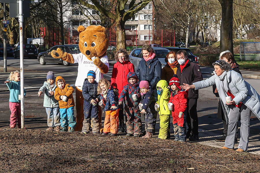 Gruppenfoto von Kindern und Dogibär beim Streuen von Wildblumen für Bienen.