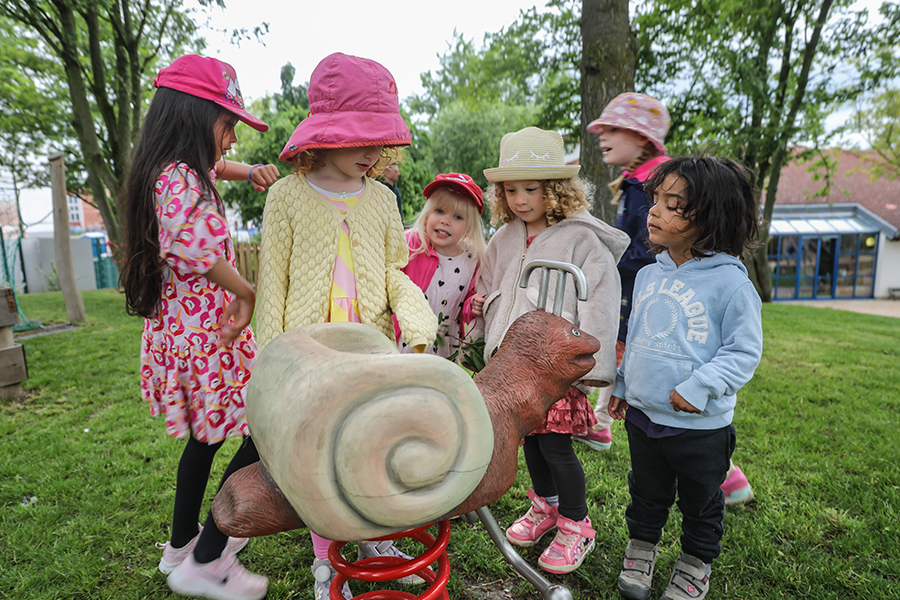 Kita-Kinder stehen neben einer Schaukel-Schnecke.