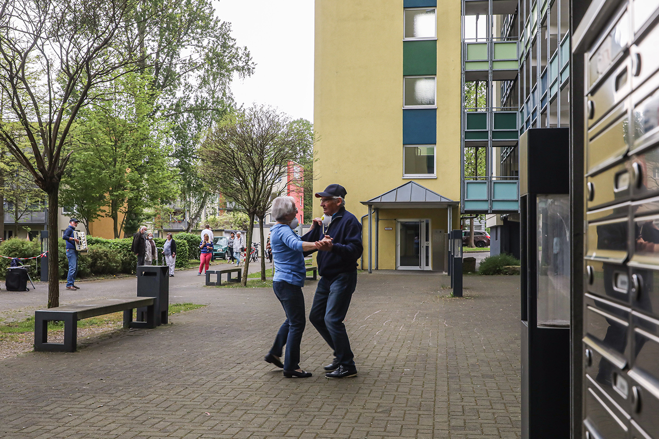 Mann und Frau tanzen während Corona vor Wohnblock.