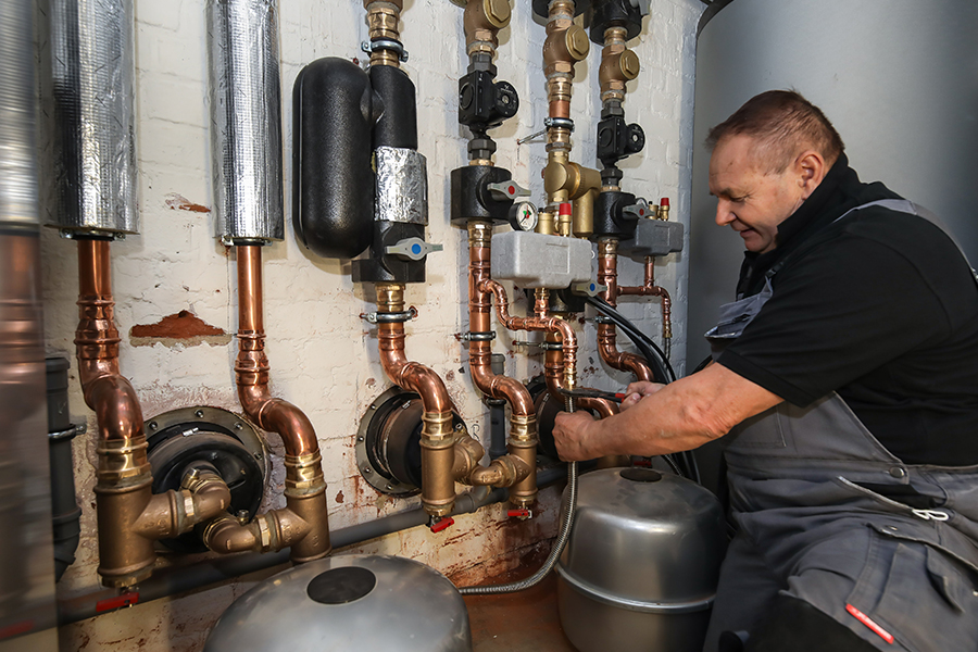 Ein Handwerker arbeitet an Rohren im Keller.