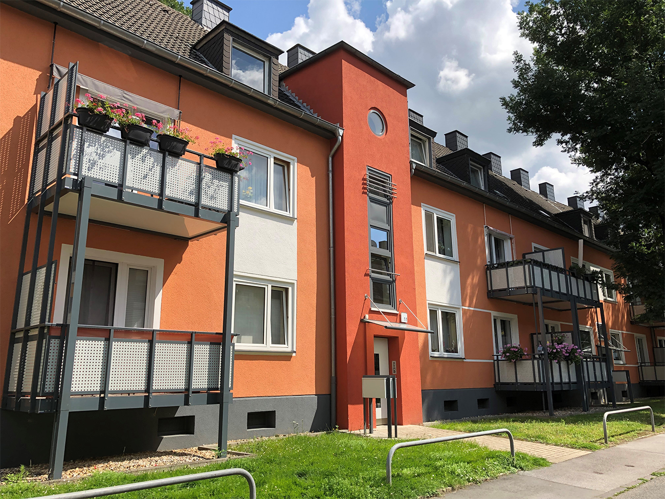 Mehrfamilienhaus mit Balkonen, auf denen im Sommer Blumen blühen.