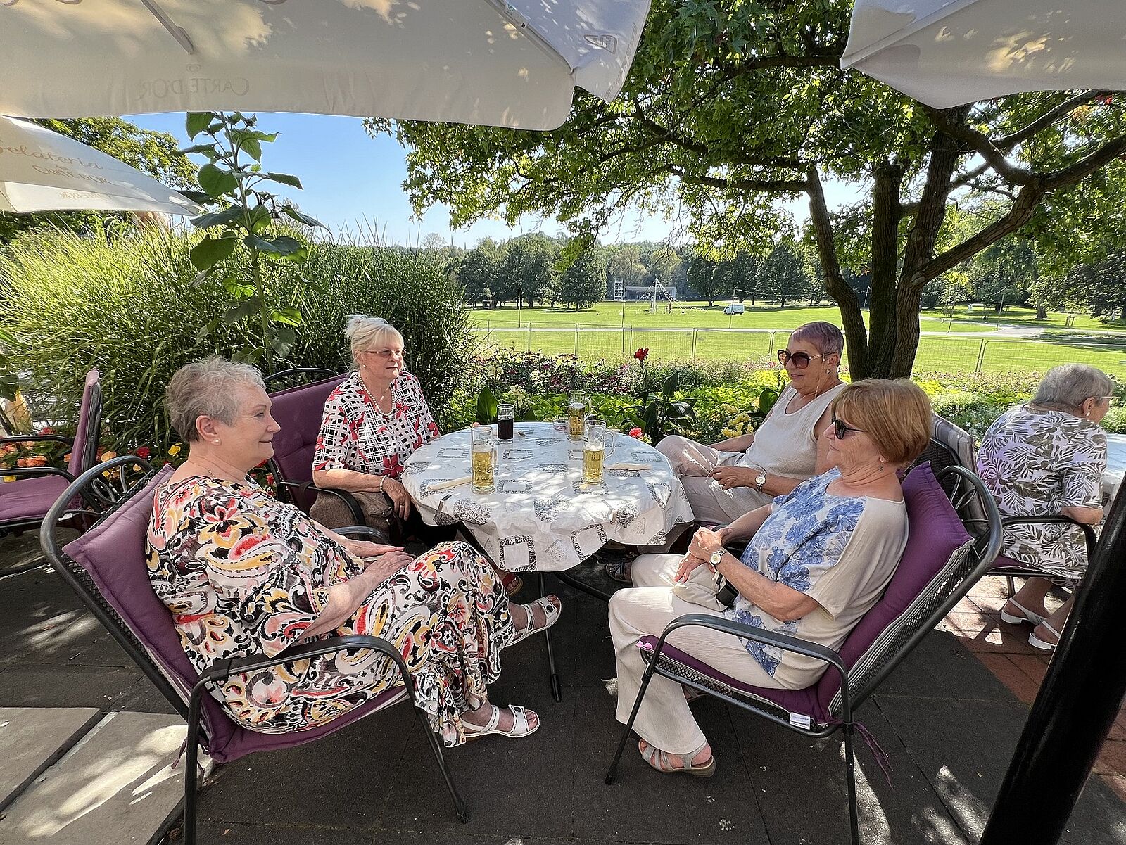 Menschen sitzen im grünen Park gemeinsam an einem Tisch unter dem Sonnenschirm.