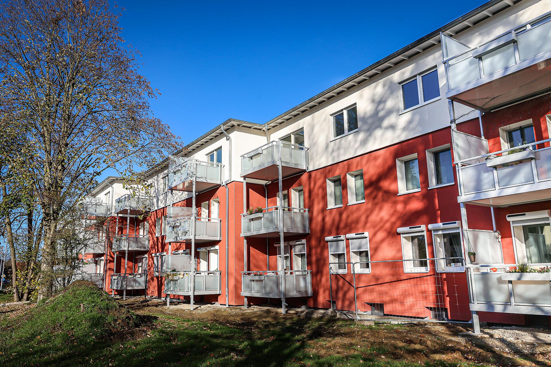 Rot-weißes Mehrfamilienhaus mit aufgestockten Dachgeschosswohnungen und neuen Anstellbalkonen