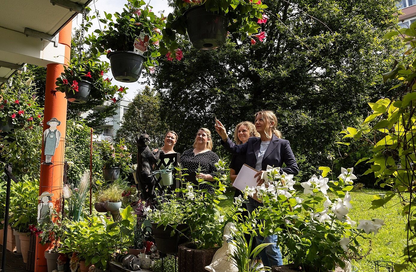 Vier Frauen stehen auf einer Rasenfläche und betrachten die üppige Blumenpracht eines Balkons