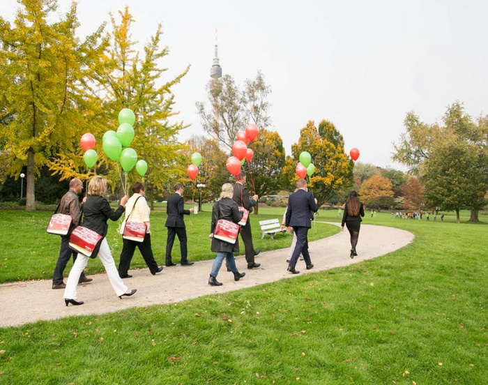 Eine Gruppe von Menschen mit Luftballons in de Hand spaziert durch den Park.