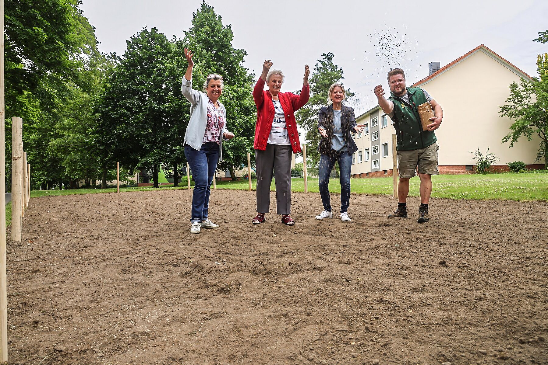 Vier Menschen stehen auf einer vorbereiteten Fläche und säen Blumensamen aus