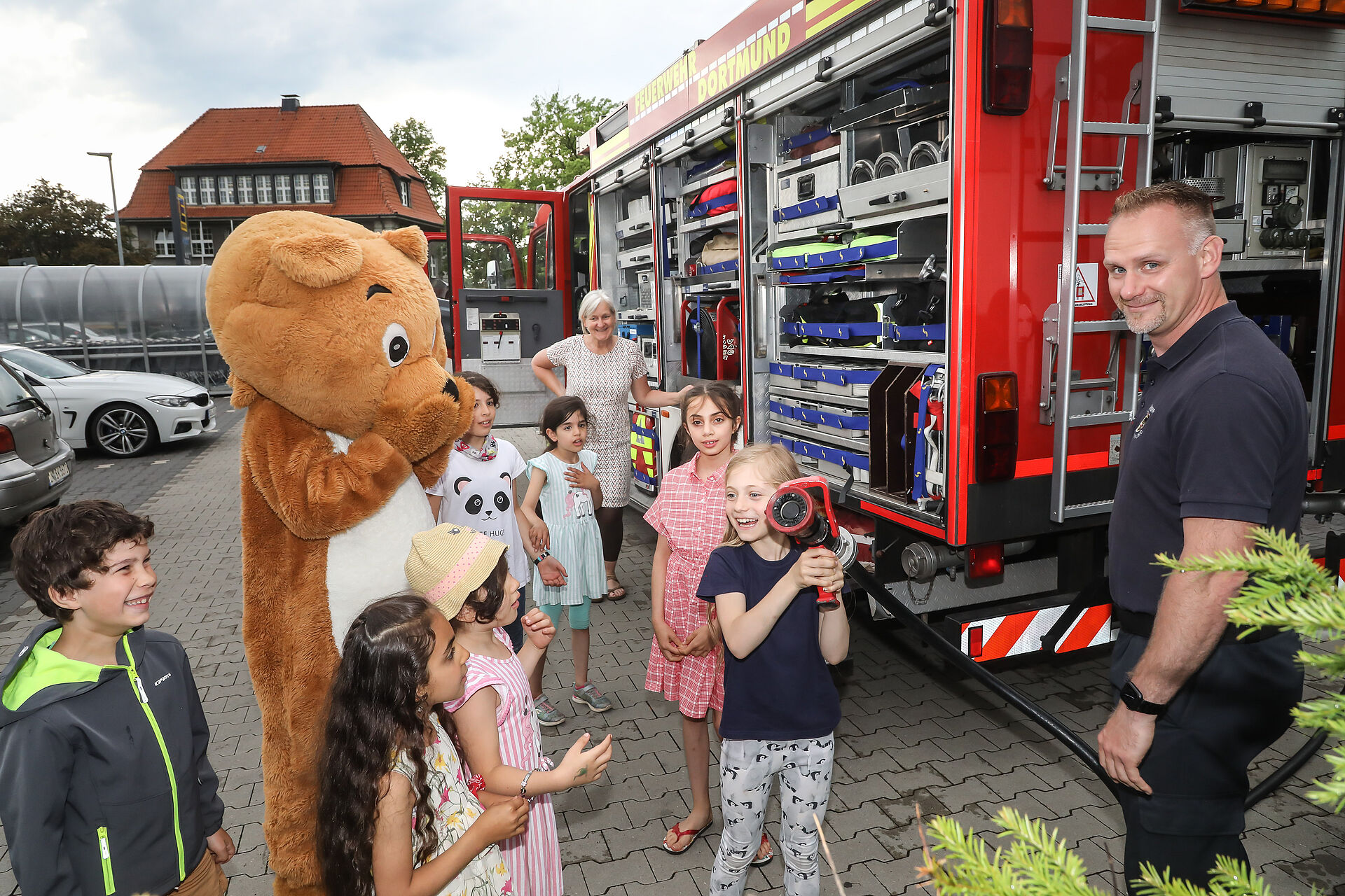 Ein Feuerwehrmann, der Dogibär und Kinder mit einem Löschschlauch