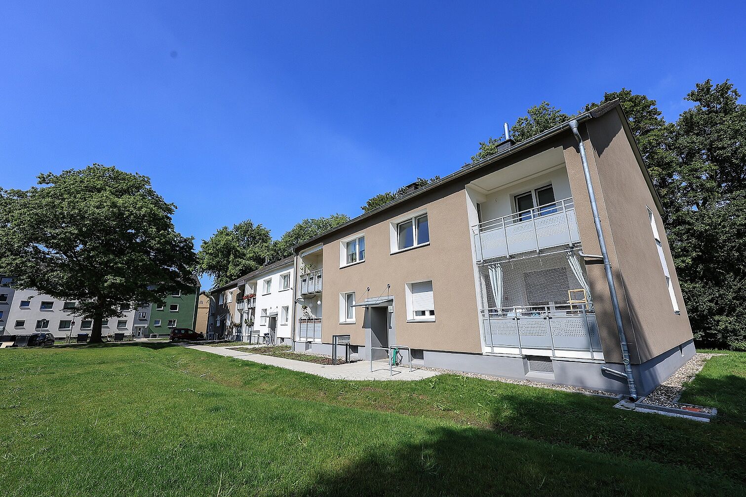 Energetisch modernisierte Mehrfamilienhäuser in weiß und braun mit Grünfläche davor und großem Baum