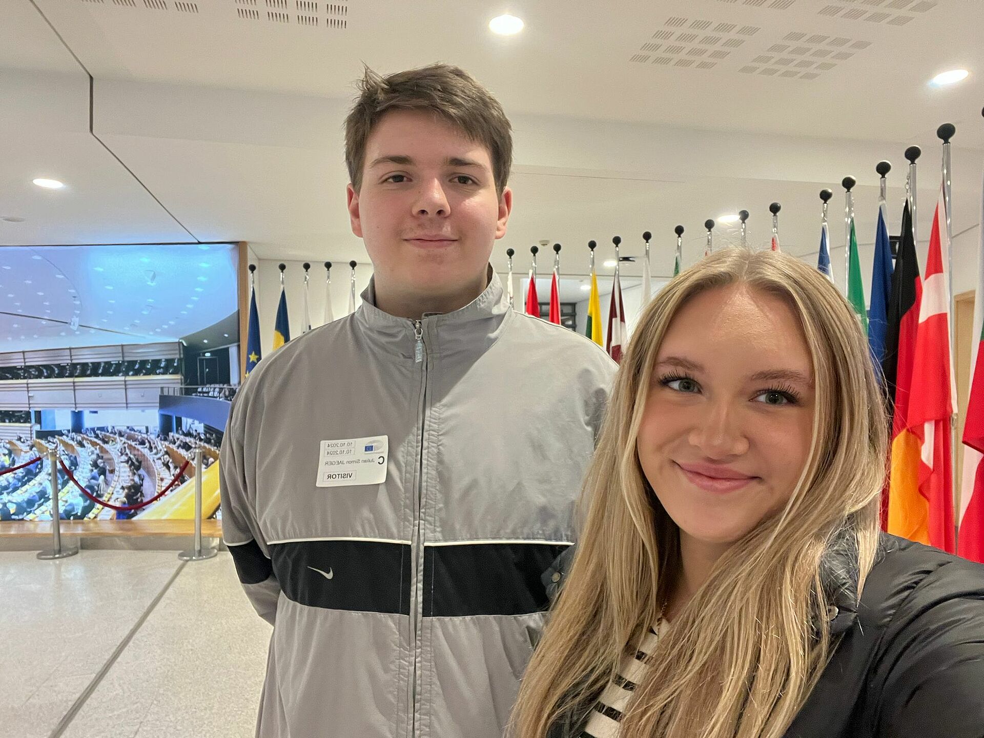 Zwei junge Menschen machen lächelnd ein Selfie vor dem Sitzungssaal des Europäischen Parlaments.