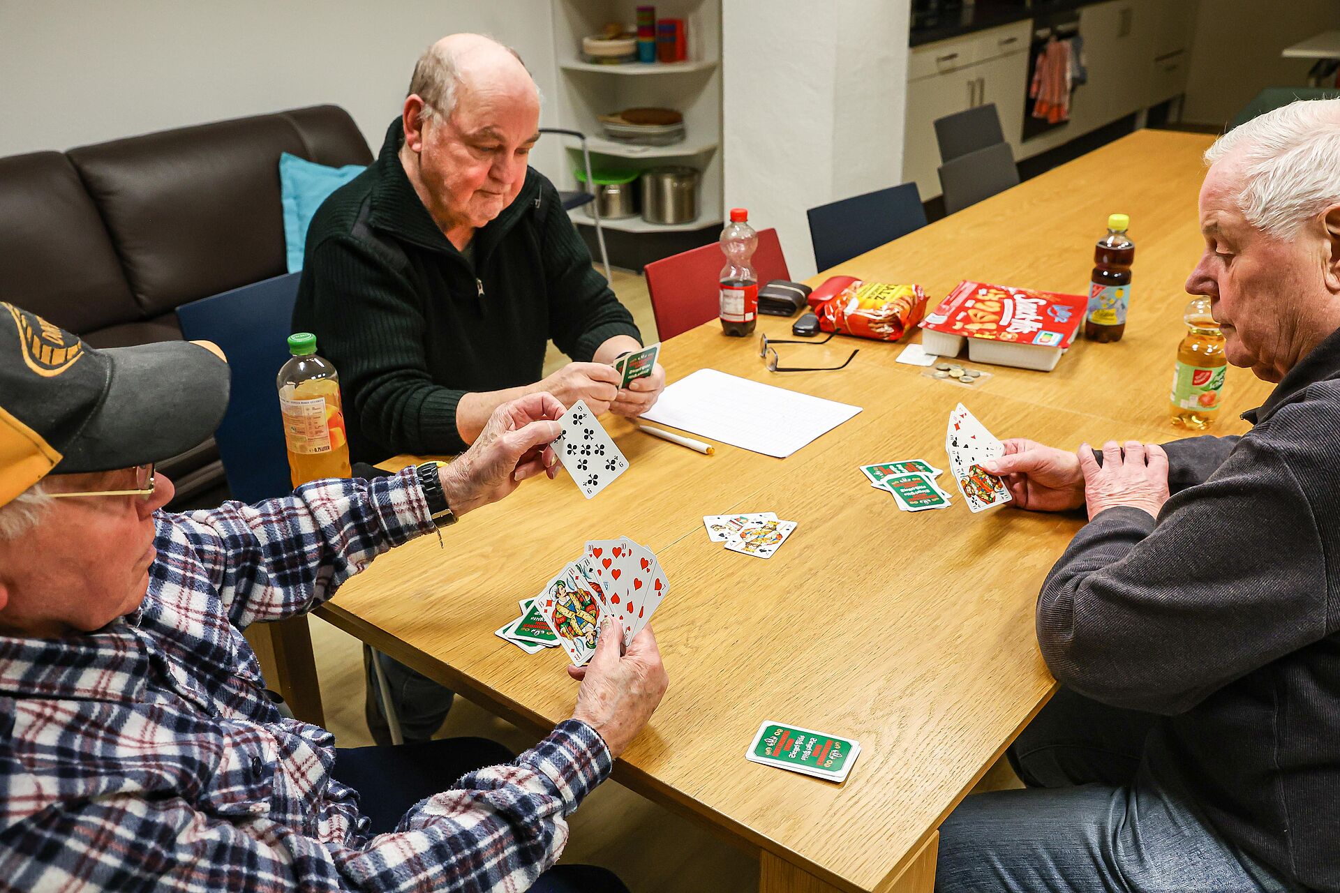 Drei Männer sitzen an einem großen Tisch und spielen zusammen Skat.