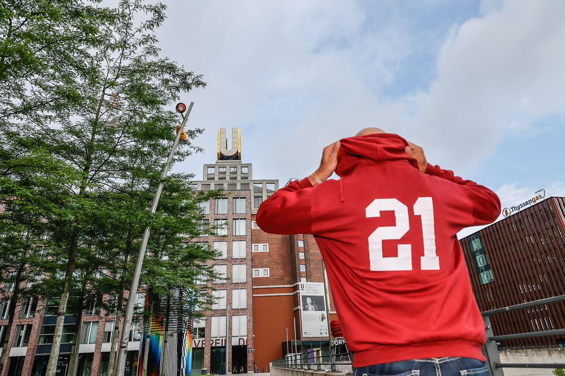 Mann mit rotem Pulli mit der Aufschrift 21 setzt seine Kapuze auf