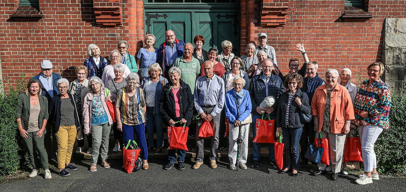 Mieterinnen und Mieter sowie Mitarbeiterinnen des Wohnungsunternehmens DOGEWO21 stehen auf den Treppenstufen vor einem historischen grünen Holzeingang auf der Zeche Zollern und schauen freundlich in Richtung des Fotografen.