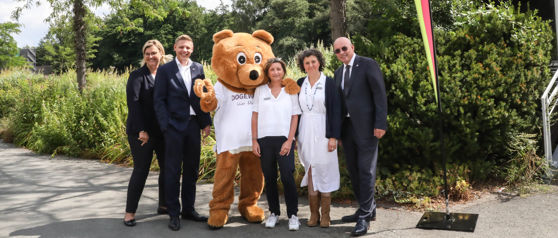 Mitarbeiter*innen von DOGEWO21 in Anzügen gemeinsam mit dem Maskottchen Dogibär